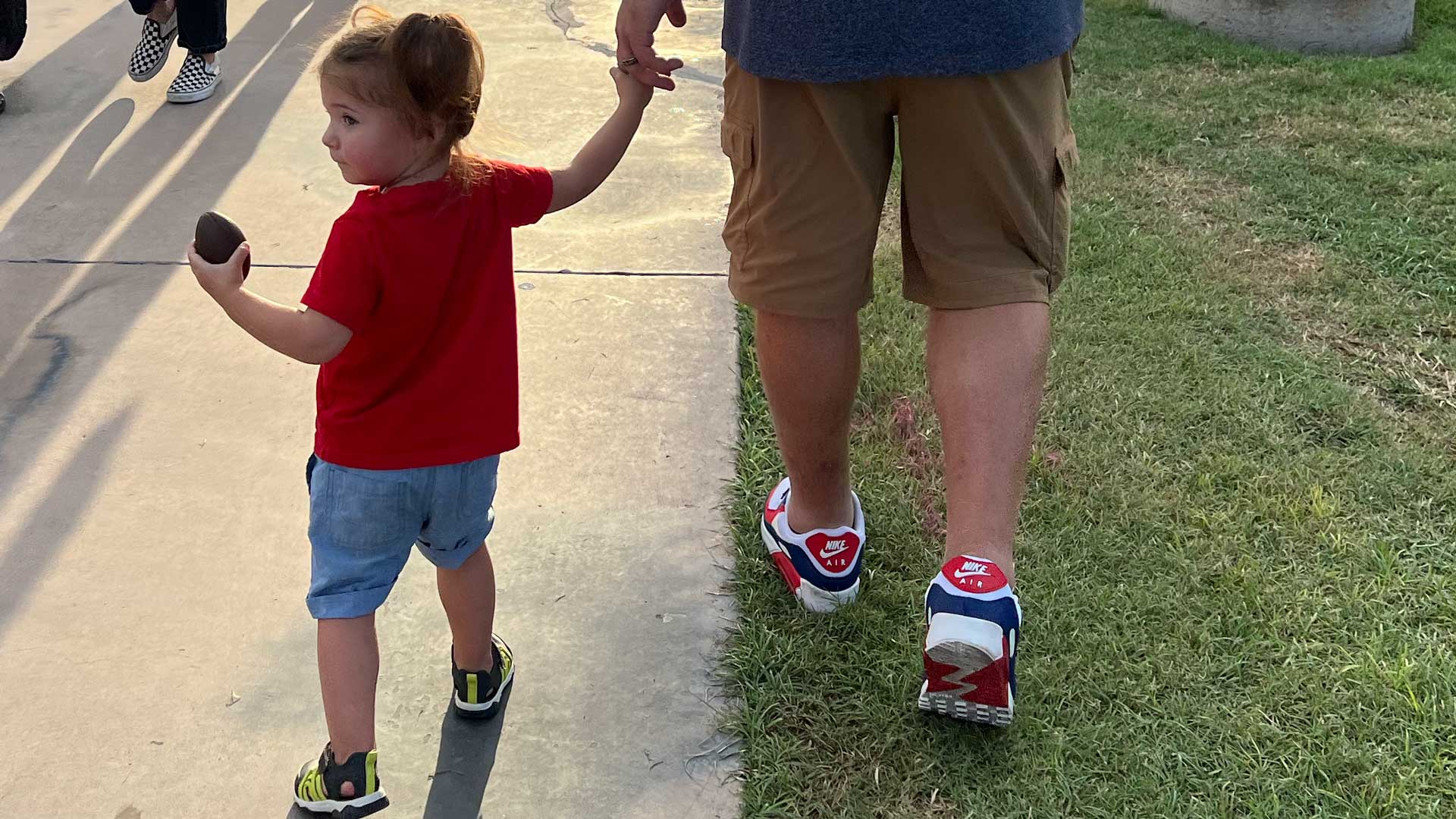 Child walking on a sidewalk holding father's hand.